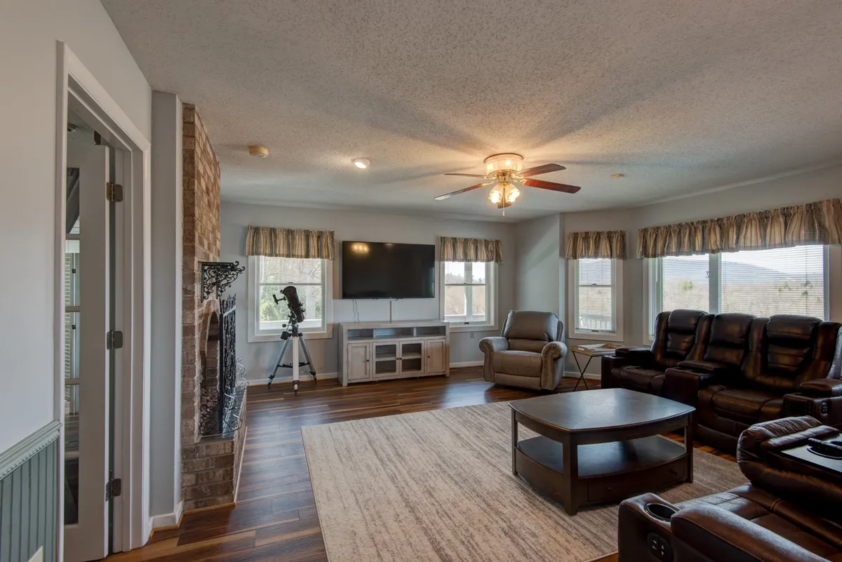 A spacious and inviting main living area featuring a beautiful stone fireplace as the focal point. Comfortable seating is arranged to foster conversation and relaxation. Large windows let in abundant natural light, while a television and a telescope hint at both entertainment and shared stargazing moments. The overall mood is warm, cozy, and perfect for gatherings.