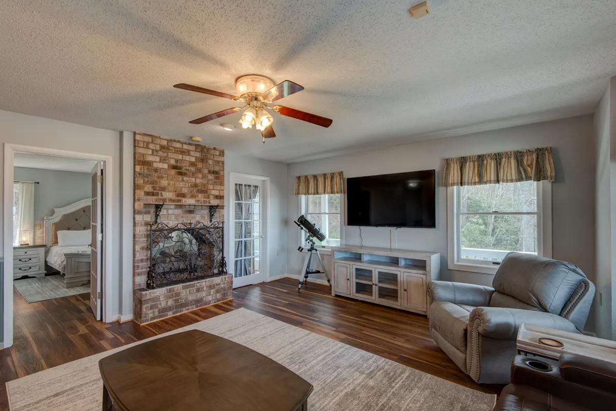 A comfortable living area anchored by a brick fireplace, a large television, plush seating, and a telescope by the window. The scene evokes cozy evenings spent streaming movies or stargazing indoors, with ample space for groups to relax together.