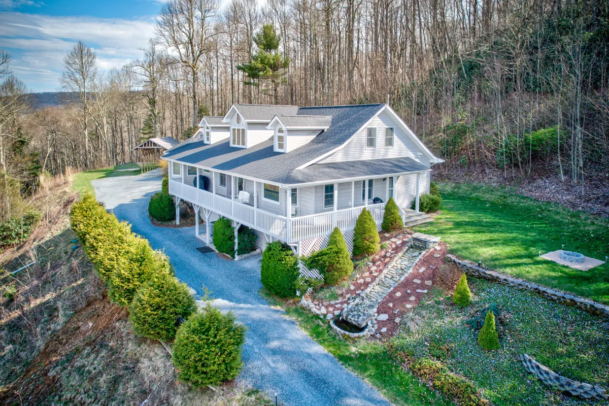 The image showcases a beautifully renovated home perched atop a hill, with a welcoming porch overlooking a meticulously landscaped yard. Rolling hills stretch into the distance, promising breathtaking sunrise views and peaceful stargazing evenings. The porch invites guests to relax and unwind, while the expansive lawn hints at space for outdoor activities and gatherings.