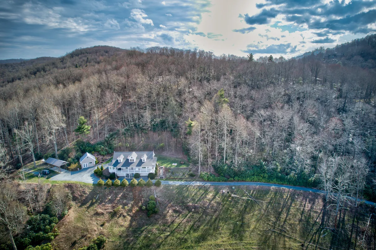 An exterior view showing the house enveloped by forest, with a lengthy driveway winding through mature trees. This perspective emphasizes the property’s seclusion and its direct connection to expansive natural surroundings, ideal for exploration.