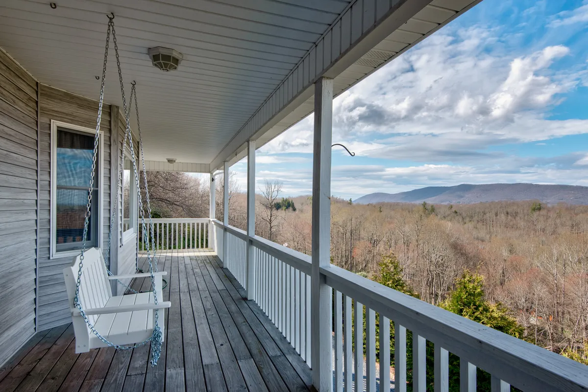 A tranquil porch scene featuring a classic porch swing, sturdy wooden railings, and sweeping views of distant mountains. The porch is covered, offering shelter and a cozy outdoor retreat ideal for relaxing and enjoying the landscape.
