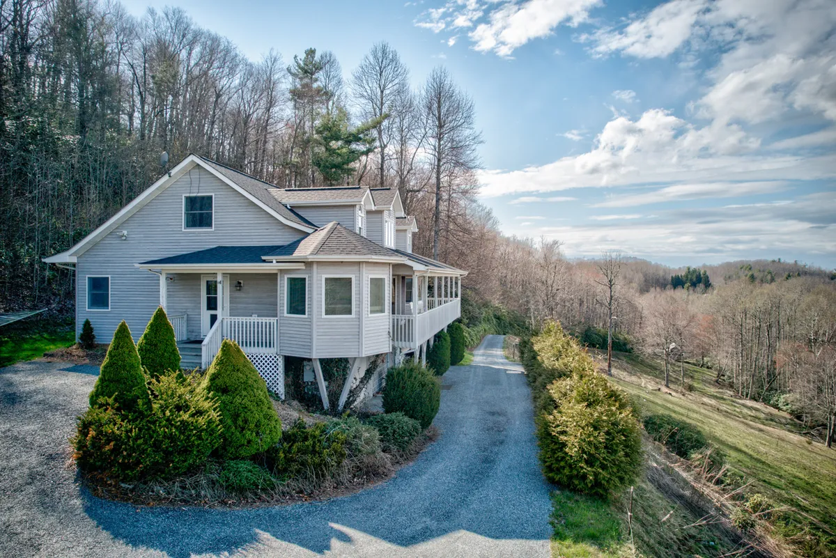 A welcoming porch scene with comfortable seating, the house's driveway, and a peaceful canopy of trees. The porch offers a spot for relaxation, morning coffee, and evening conversations, all set within the serene landscape.
