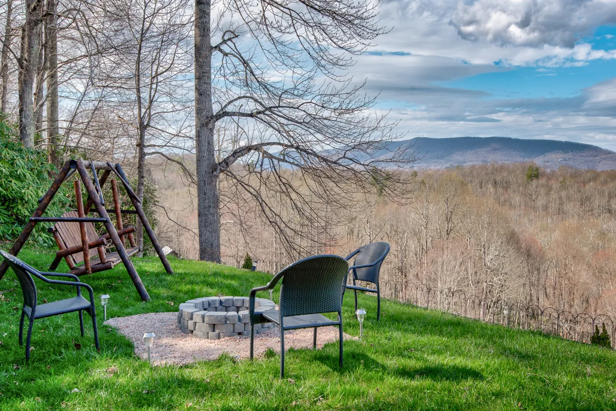 A spacious outdoor area with a welcoming fire pit surrounded by comfortable chairs, a swing set nearby, and panoramic mountain vistas beyond. The setup encourages gatherings, storytelling by the fire, and leisure under the open sky.