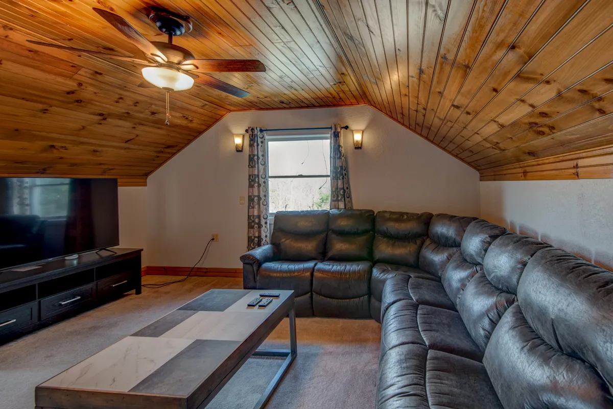 A spacious loft area showcases a large leather sectional sofa, a big-screen television, and a wooden coffee table—perfect for movie marathons, board games, or casual relaxation with family and friends.