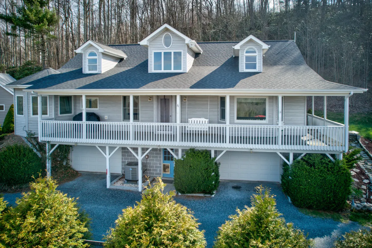 A welcoming front porch with dormer windows and a landscaped yard invites guests to relax outdoors. The porch suggests a comfortable spot for people to unwind while watching their pets play in the yard.