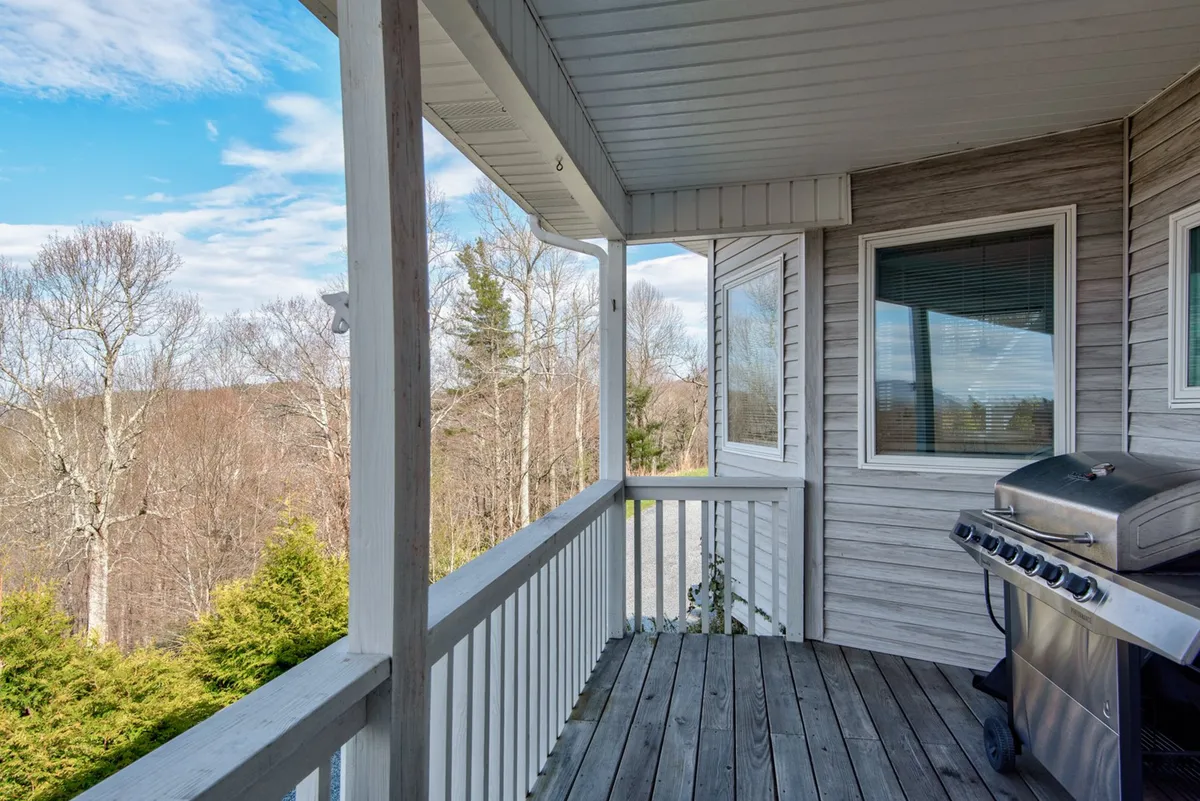 A peaceful outdoor balcony scene featuring a sturdy railing, barbecue grill, and dense greenery. The vantage point hints at secluded relaxation spaces where one can enjoy nature, sunsets, or al fresco meals.