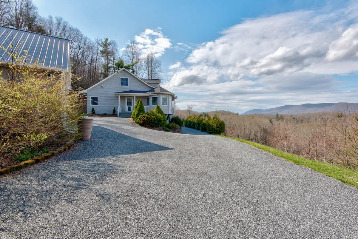 This image presents a wide view of the home set against a scenic mountain backdrop, with the driveway and lush trees creating a sense of arrival and seclusion. The setting highlights the expansive property and its tranquil natural surroundings, ideal for large family gatherings and outdoor activities.