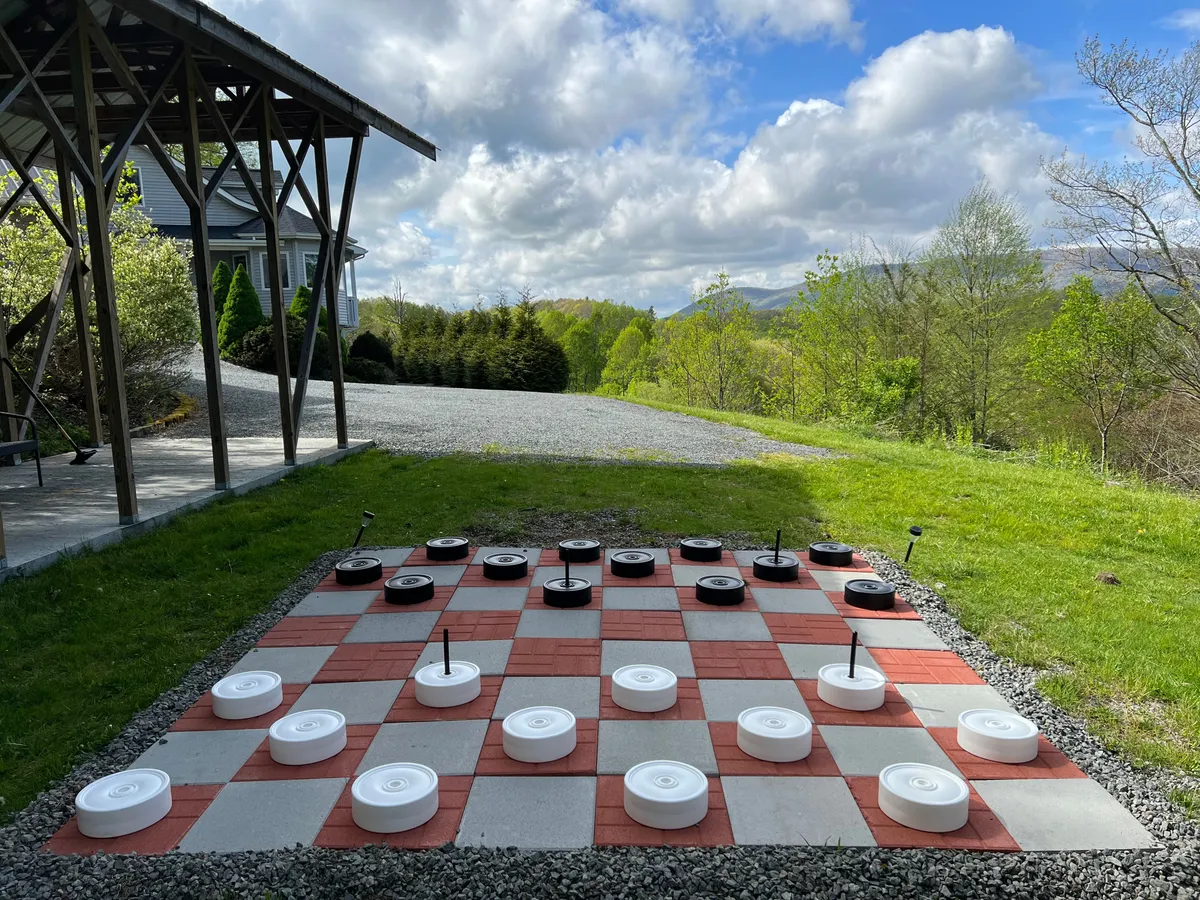 This exterior shot captures a large outdoor checkers board set against a scenic mountain view. A wooden structure nearby hints at a welcoming gathering space, while the open sky and lush surroundings suggest ample room for family play and relaxation.