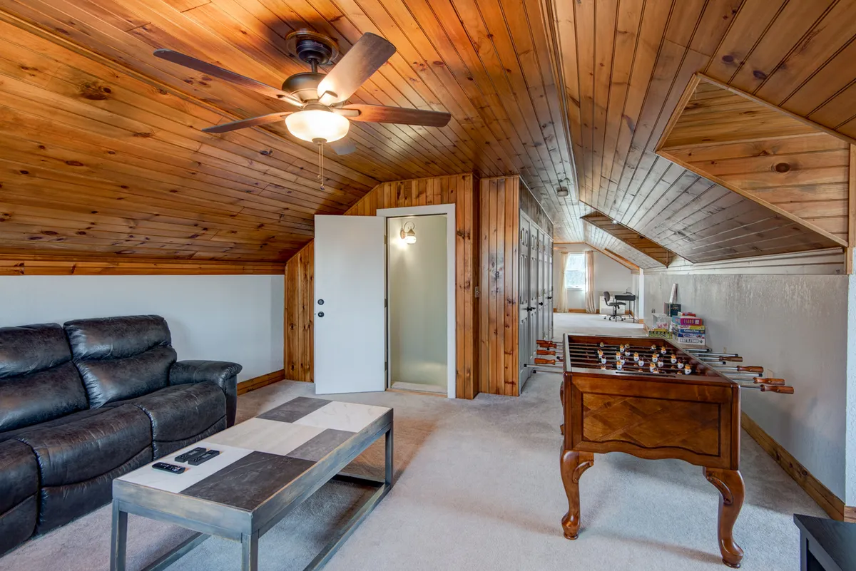 This image features a cozy leather sofa, a wooden coffee table, and, most prominently, a foosball table in the foreground, all under a warm wooden ceiling. The space feels inviting and lively, ideal for both relaxing and interactive activities.